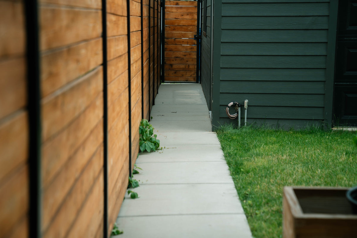 Concrete side path beside a cedar fence and dark siding
