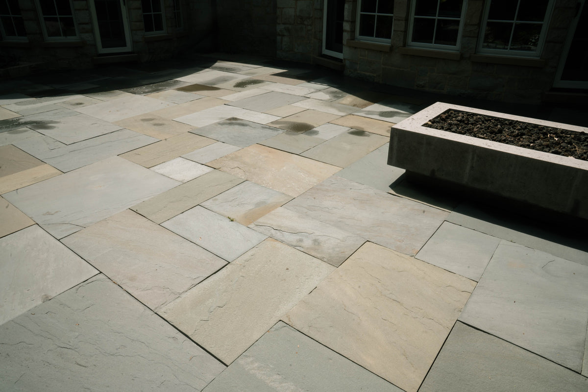 Stone patio with a rectangular fire bowl outside a stone home